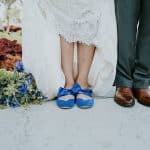 Bride wearing blue ballet flats with ankle straps, standing in lace dress next to groom