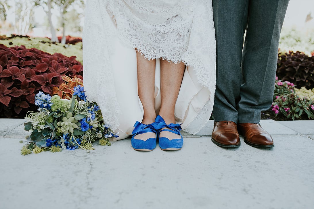 Bride wearing blue ballet flats with ankle straps, standing in lace dress next to groom