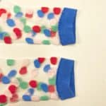 Pair of transparent mesh socks with multicolor dots and blue cuff toe and heel displayed flat