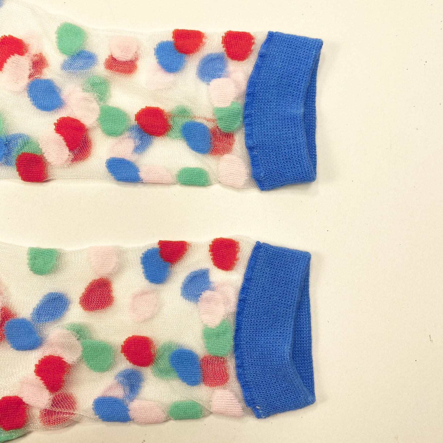 Pair of transparent mesh socks with multicolor dots and blue cuff toe and heel displayed flat