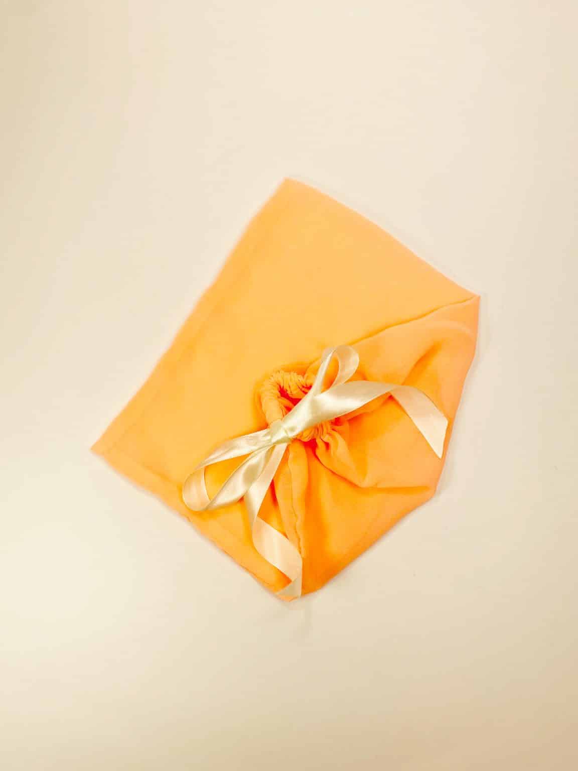 Peach colored cotton dust bag for shoes tied with ivory satin ribbon