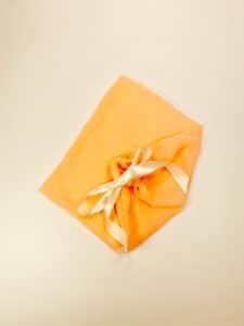 Peach colored cotton dust bag for shoes tied with ivory satin ribbon
